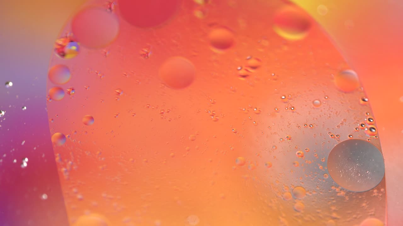 Macro oil drop in water. Yellow, red, orange, violet bubbles background. Holographic liquid