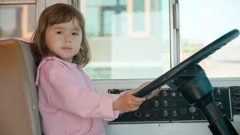 3-year-old little girl sitting in the driver's seat pretends to drive real old bus