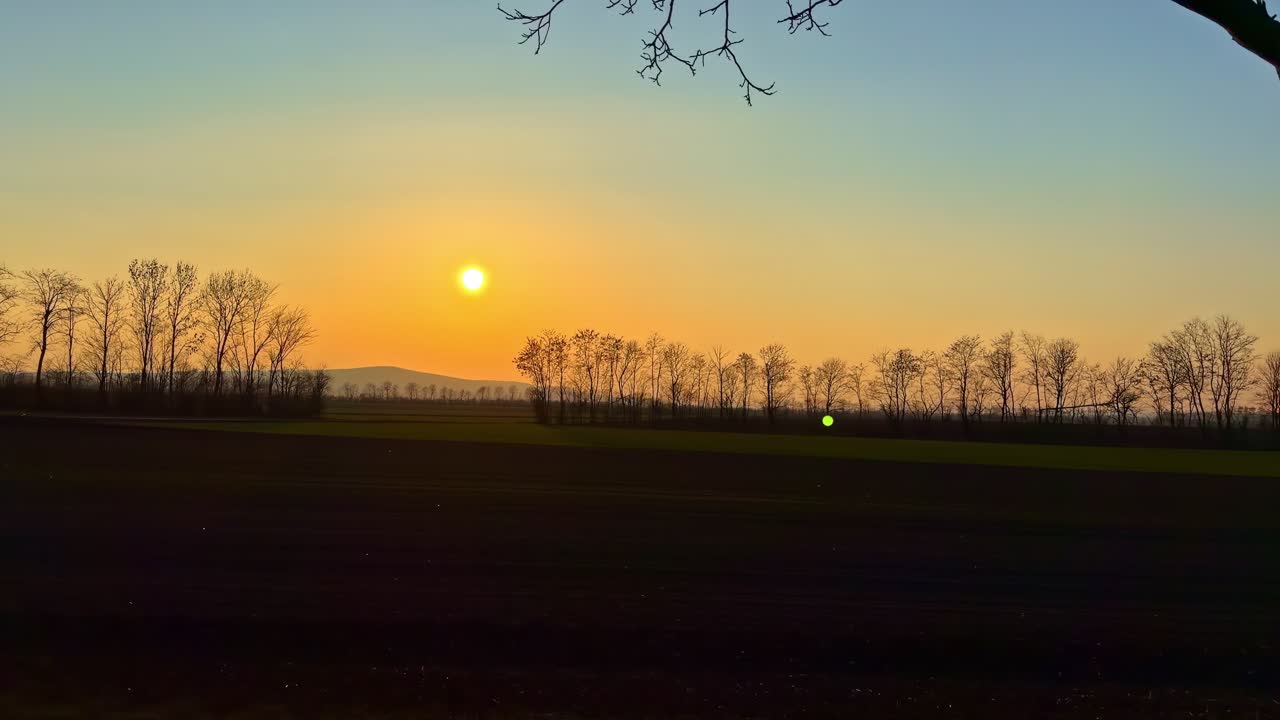 Udsigt til farverig himmel med solnedgang fra et bevægende bilvindue.