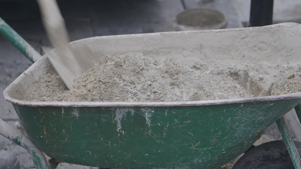 Spade som blander tørrsement og sand i en grønn trillebår