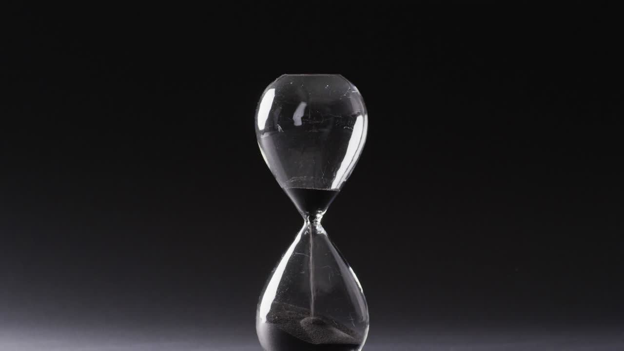 Video of hourglass with sand pouring, copy space on black background