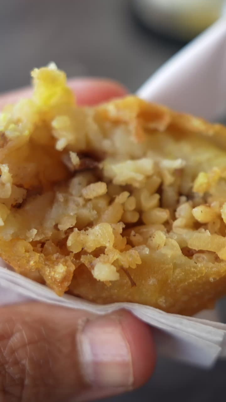 Savor the crispy texture of a papa rellena in this vertical video close-up. The golden-brown crust and rich potato filling are captured in detail, perfect for social media stories