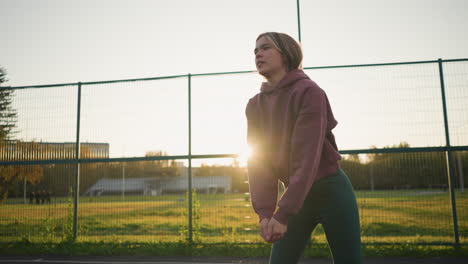 young lady playing volleyball in an open field with bright sunlight, action shot of her striking the ball with an energetic, focused posture, the background features a green field with buildings