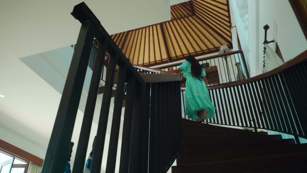 한 소녀가 파란색 긴 드레스를 입고 나무 계단을 맨발로 올라간다.