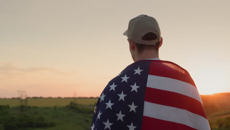 un hombre con una bandera estadounidense en los hombros admira el amanecer sobre un pintoresco valle. concepto del día de la independencia