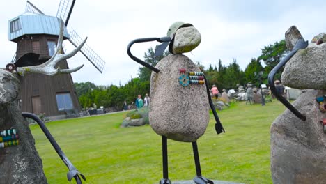 stone lamb sculptures in saaremaa estonia at lambakogu that have medals. saluting to something while holding up their metallic arms during summer. an old wooden windmill in the background with windows