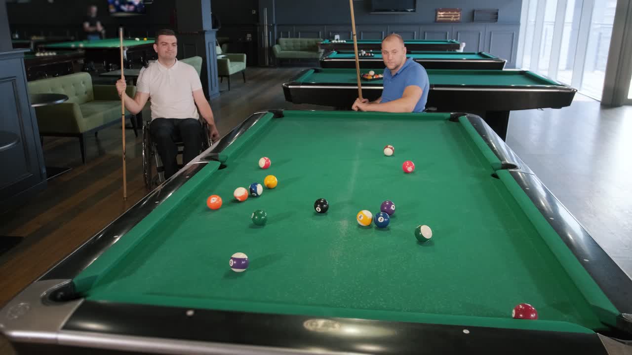 Adult men with disabilities in a wheelchair play billiards in the club