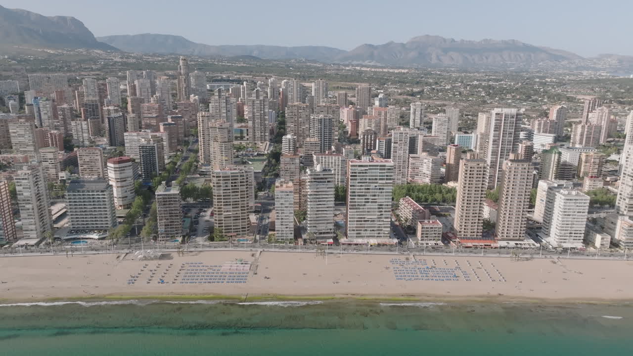 Lateral drone shot of Levante Beach in Benidorm, moving left to right with tall skyscrapers and clear skies