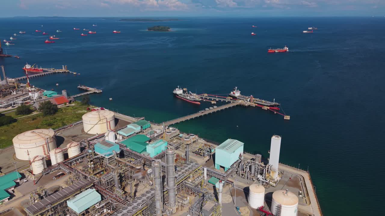 Aerial view of the Petronas Methanol Plant in Labuan, Malaysia, showing large industrial structures, pipelines, storage tanks, and tankers docked along the pier in the deep blue sea