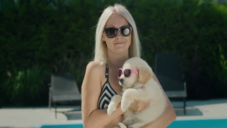 A-woman-in-a-bikini-holds-a-blonde-puppy-in-sunglasses-in-her-arms.-Summer-and-vacation-with-a-pet-concept