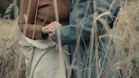 couple holding hands standing close to each other, in a field with tall grass