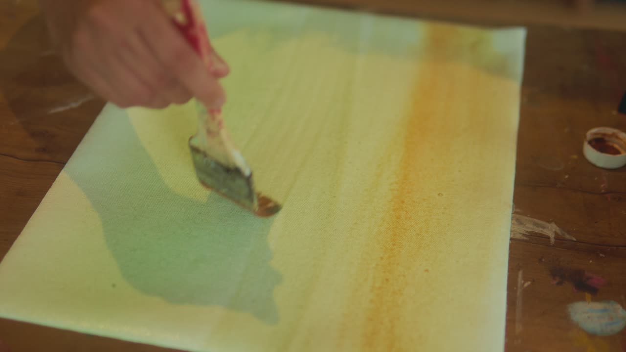 Primo piano di un pennello che crea una pennellata di colore caldo su carta, dettaglio di un processo artistico creativo indoor.