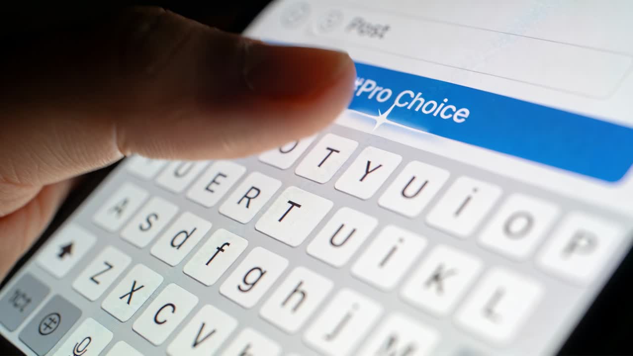 Tapping right thumb appearing on screen composing post in low-light close-up, selecting #Pro Choice