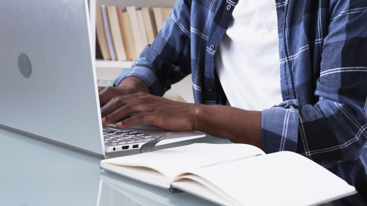 Man typing on laptop at home, open notebook on desk, working remotely