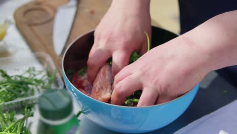 man is mixing meat pieces with spices and herbs in metal bowl. the wooden surface outside. barbeque time. shot in 4k