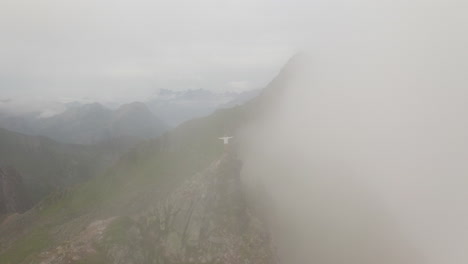 Revelación-Aérea-Alrededor-De-Un-Joven-Excursionista-Parado-En-La-Cima-De-La-Montaña,-Moviéndose-A-Través-De-Las-Nubes-Fløya-Y-Djevelporten-Sobre-Svolvær-En-Lofoten,-Noruega,-Imágenes-Aéreas