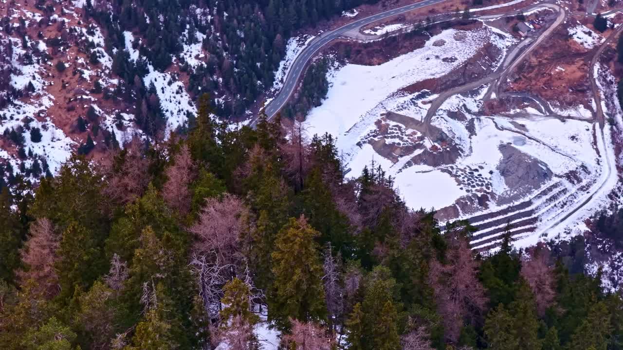 Sorvolo aereo di una pineta che rivela una strada di montagna innevata a Nauders, Austria, paesaggio di trasporto invernale