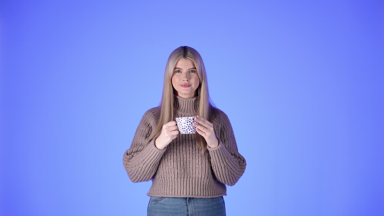 A young blonde woman drinking from a mug against a blue background
