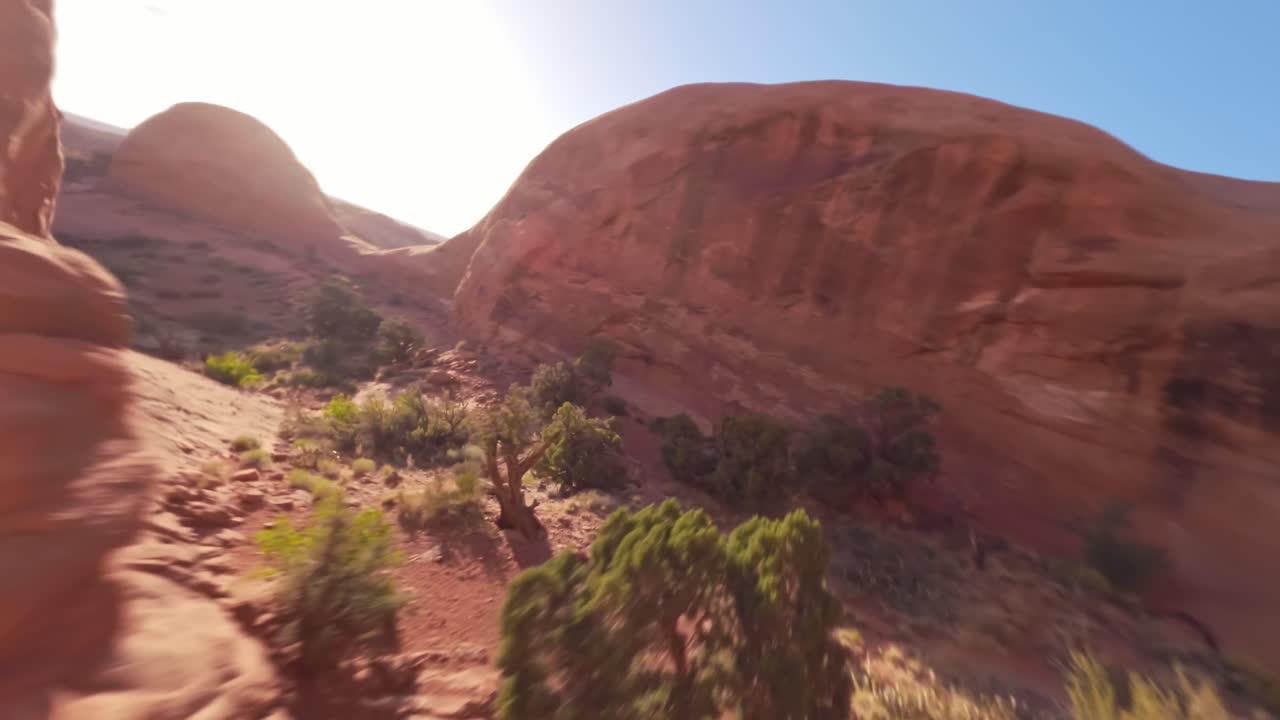 A low-flying FPV drone flying towards and through the red sandstone Funnel Arch in the sandy and rocky desert of Moab Utah