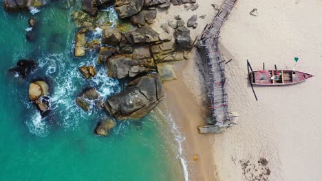 sandy beach with rocks old wooden pier and turquoise seawater lapping on the sand