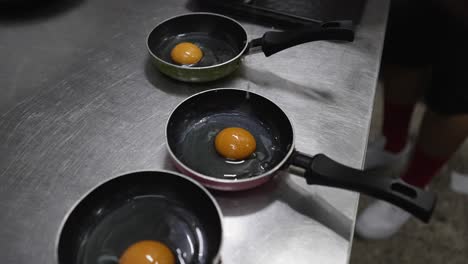 chef cracking egg on frying pan in restaurant kitchen, closeup on hands