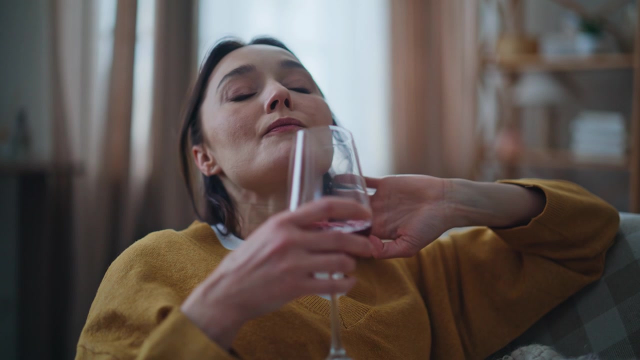 Sad brunette sipping red wine sitting alone on sofa closeup. Upset woman home