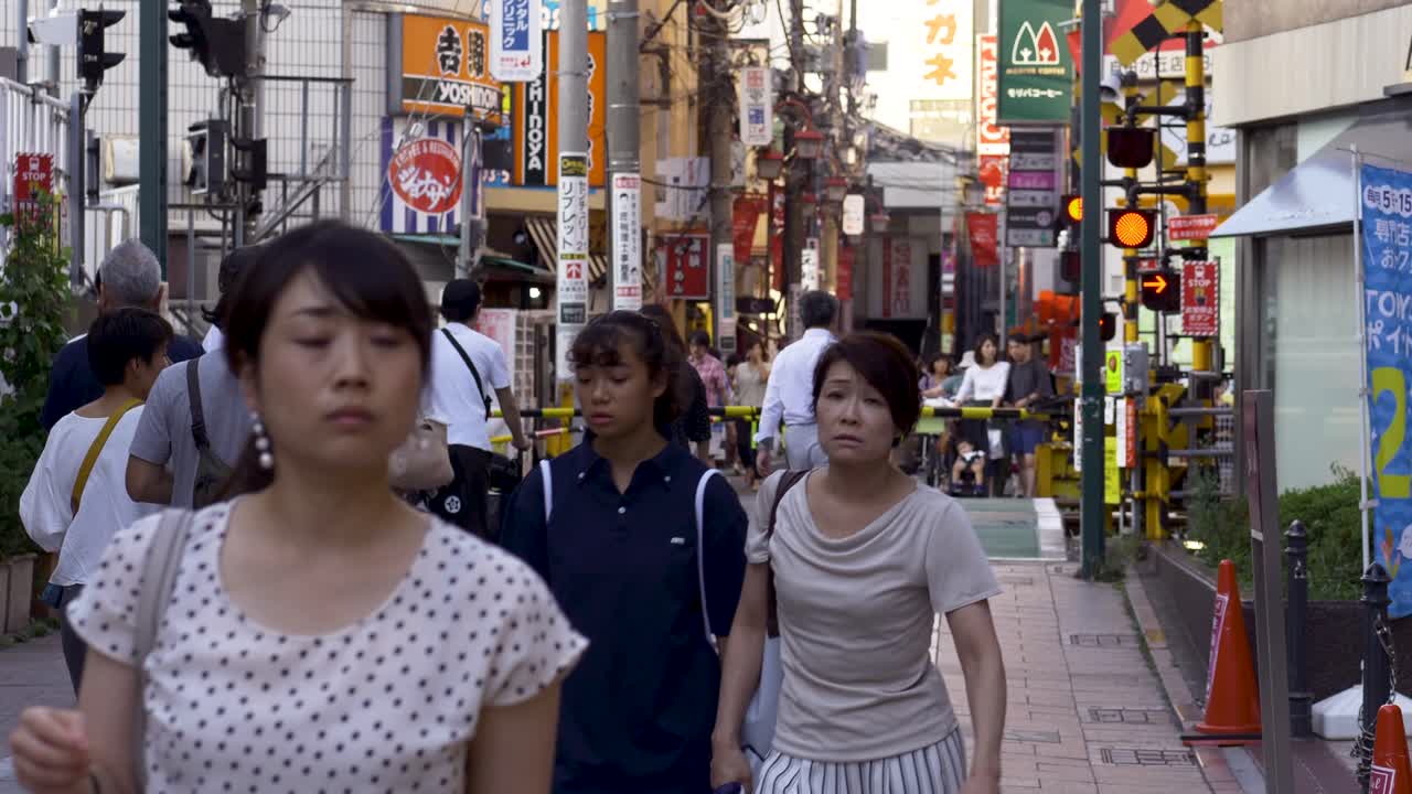 View of train crossing in the heart of Jiyugaoka’s high street, Tokyo, with shoppers and pedestrians passing by and waiting for the barriers to open.