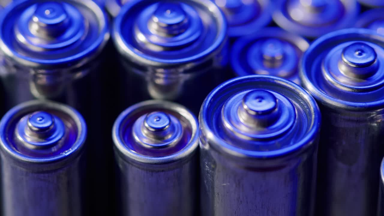 Silver batteries AA and AAA in neon light close-up. Double-A battery is a standard size single cell cylindrical dry battery. Batteries are common in portable electronic devices. An AA battery is composed of a single electrochemical cell that may be either a primary battery or a rechargeable battery.