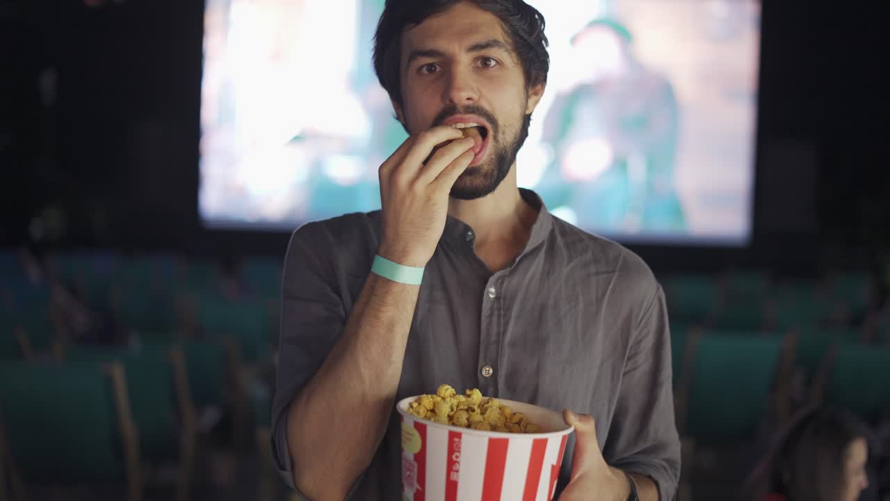 un tipo con barba come palomitas de maíz en el cine de verano, sonriendo a la cámara