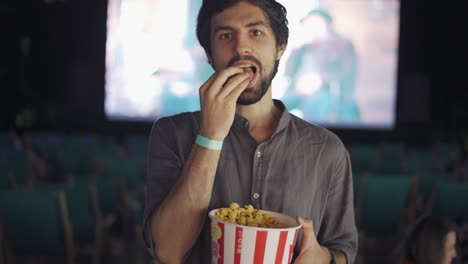 a bearded guy eats popcorn at the summer cinema, smiling to the camera