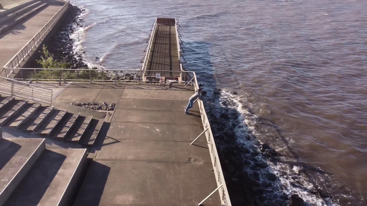 toma de órbita aérea de un joven parado en una barandilla frente a la orilla del río durante la puesta de sol dorada en buenos aires