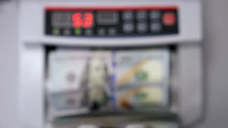 automatic machine counting dollar banknotes. modern banking activity. blurred background. hand is taking a pack of counted dollar bills from the counter machine.