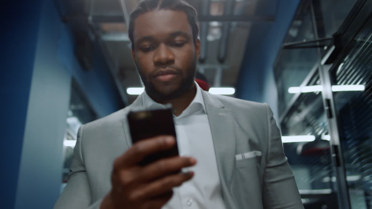 African american man walking in office. Afro man texting message in corridor