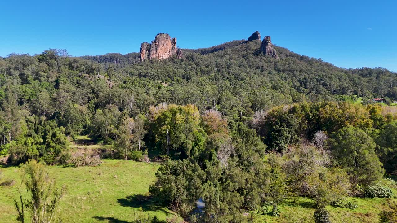 Aerial footage captures Nimbin's lush greenery and rugged hills under clear blue skies, showcasing natural beauty and tranquility