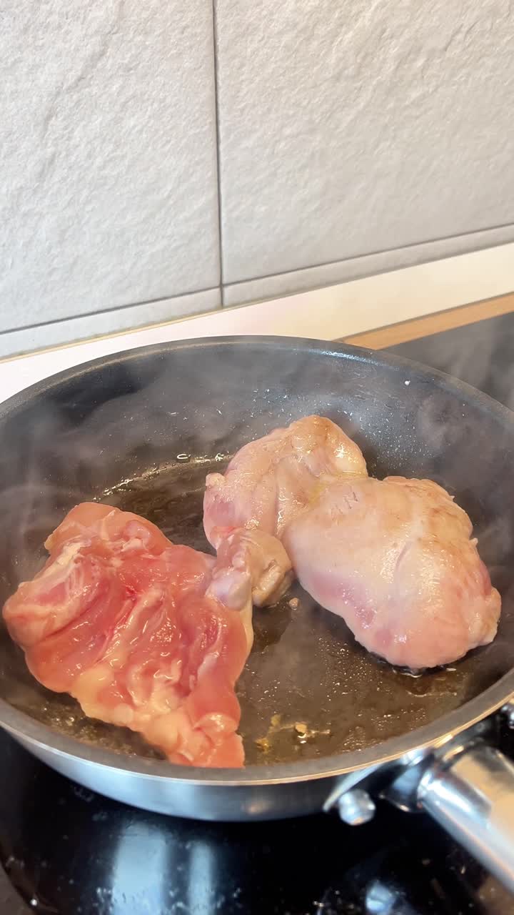Due pezzi di carne stanno cuocendo in una padella su un fornello. La padella è calda e la carne sta rosolando.