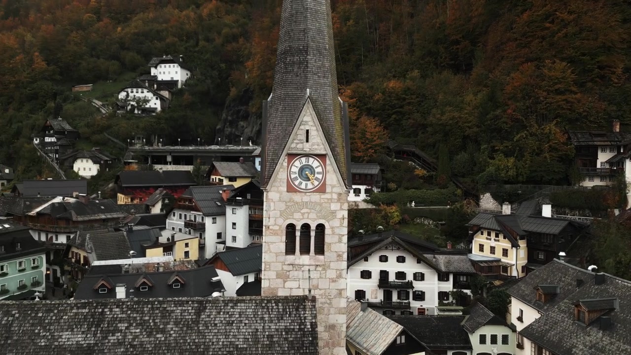 Una vista pintoresca de un pueblo histórico enclavado en las montañas que muestra una alta torre de iglesia y casas alpinas tradicionales rodeadas de follaje otoñal