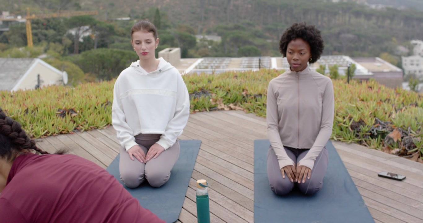 African American maroon coach guiding women kneeling on deck, gesturing for calm with mats, bottle