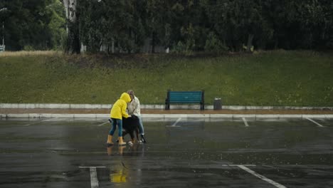 feliz mujer rubia en una chaqueta blanca junto con su hija en una chaquette amarilla jugando con su gran perro negro durante la lluvia en el parque