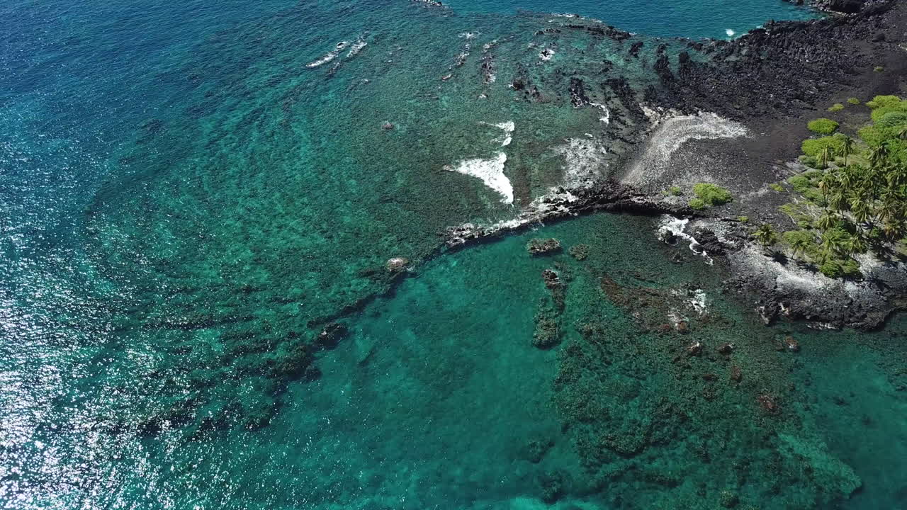 aguas cristalinas y azules frente a la playa de arena negra bordeada de palmeras en la isla grande de hawaii, panorámica sobre rocas y arrecifes