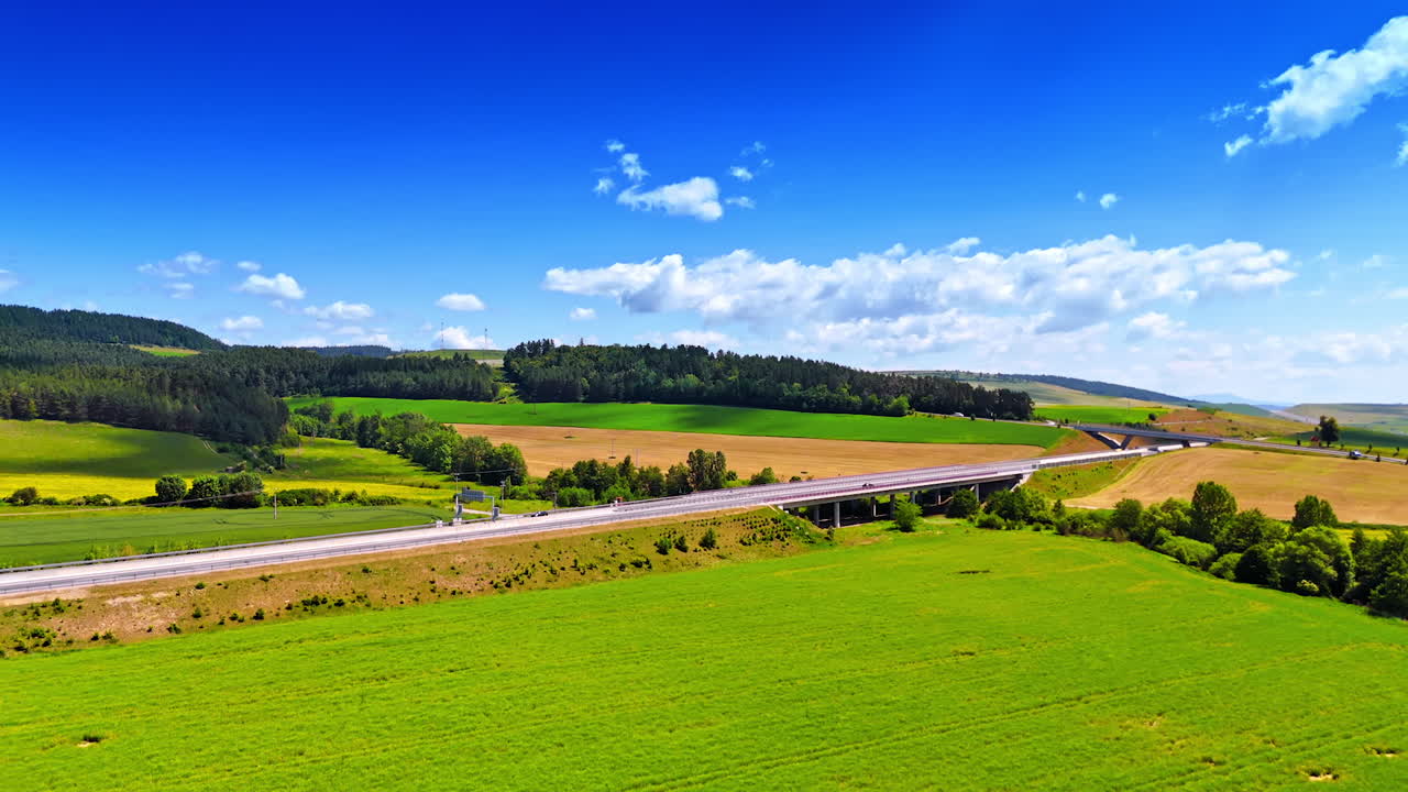 Expansive green landscape near highway. A vibrant green field stretches under a clear blue sky, with a highway cutting through the scenic countryside