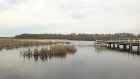 Unglaublicher-Drohnenflug-über-Wasser-Zu-Einem-Fischerboot-Auf-Einem-Steg-Bei-Frühlingssonnenuntergang-Auf-Einem-See-An-Einer-Perfekten-Hochzeitslocation-In-Brandenburg-Deutschland