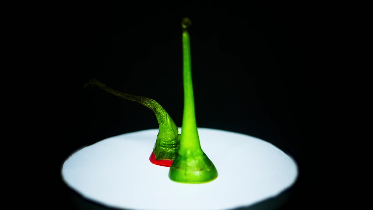 흰색 접시에 있는 녹색 및 빨간색 칠리 고추 꼭대기, 검정색 배경으로 회전 - 닫기