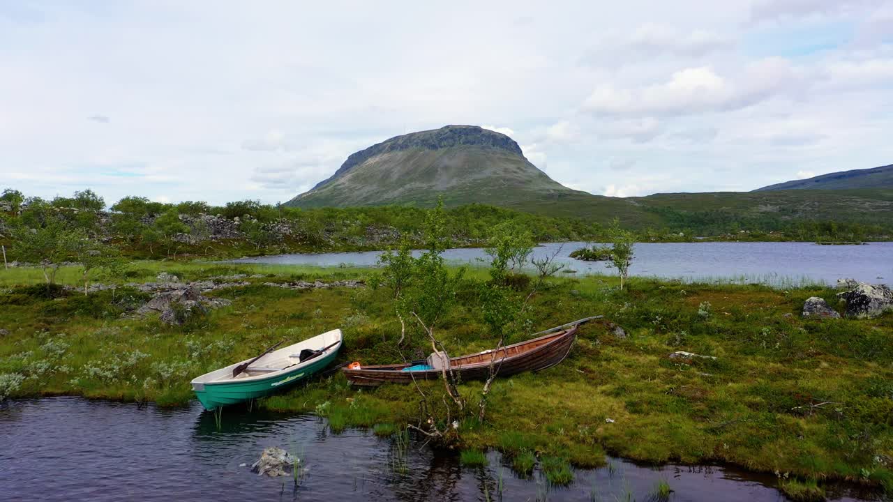 Aerial view over canoes on lake Tshahkajarvi, towards the Saana fell, on a overcast, summer day, in Kilpisjarvi, Enontekio, Lapland, Finland - Rising, drone shot