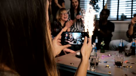 niña tomando una foto de teléfono inteligente de una fiesta de cumpleaños con fuegos artificiales brillantes y amigos multiétnicos aplaudiendo en cámara lenta