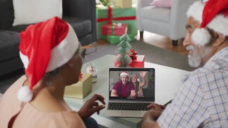 Happy-senior-african-american-couple-on-video-call-on-laptop-caucasian-couple-at-christmas-time