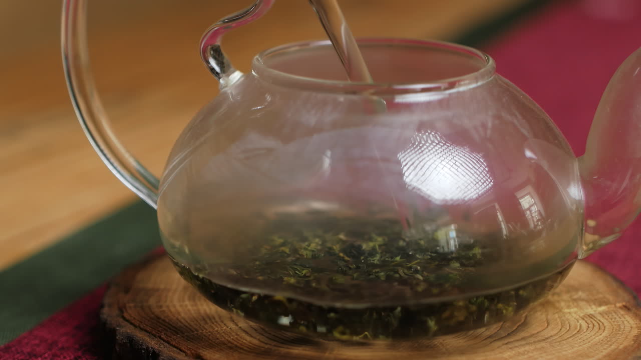 vertiendo agua caliente sobre el té verde en una tetera de vidrio