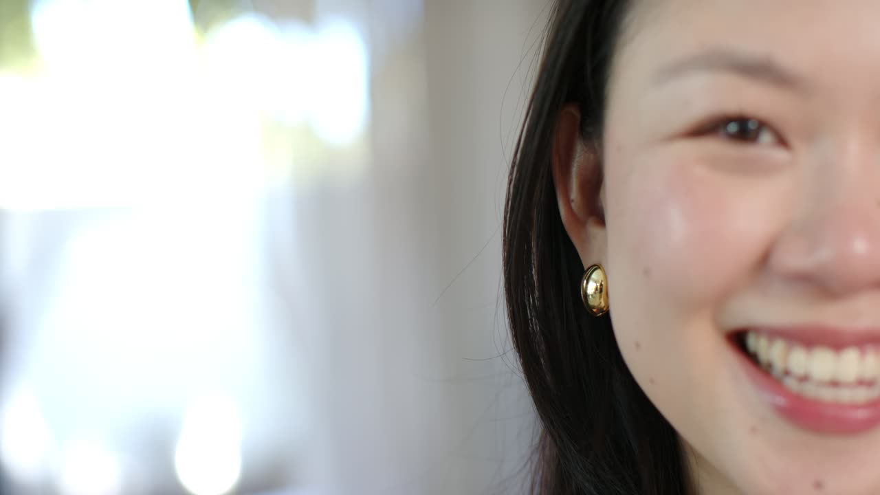 Donna asiatica che reagisce fuori campo, sorridendo, ridendo, mostrando un orecchino vicino alla finestra, spazio per la copia