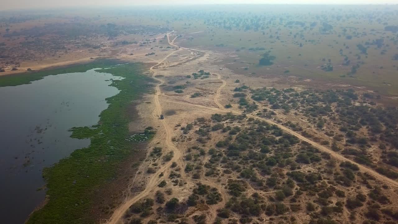 Safari tour vehicle travels dusty trails near green riverbanks in Murchison Falls National Park Uganda during dry season under hazy midday light