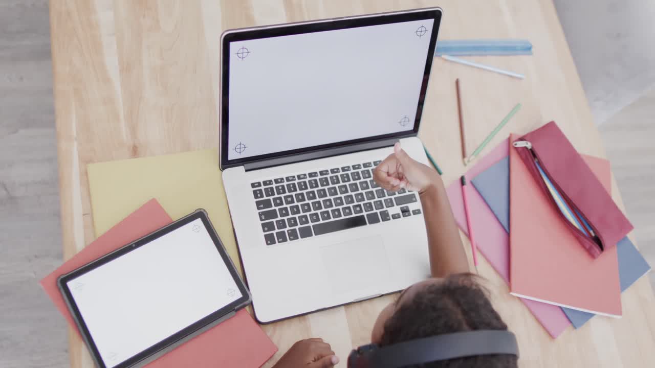 una chica afroamericana sentada en la mesa, usando una computadora portátil y una tableta con espacio para copiar, en cámara lenta.