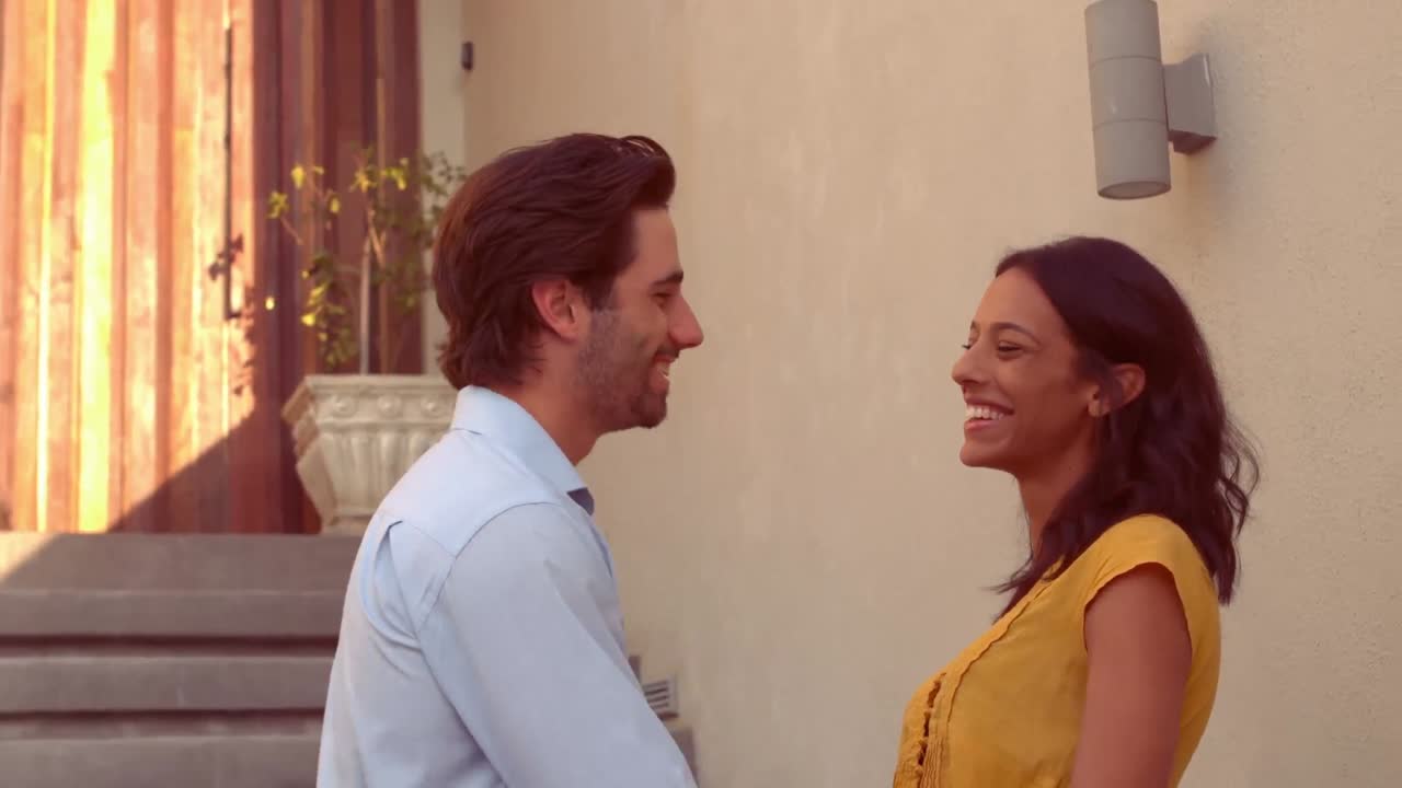 una pareja hispana sonriente frente a su nueva casa.